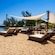 Wooden beach loungers with cushions under shade structures on a sandy beach near the ocean